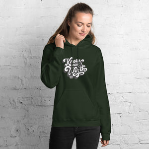 AG - Woman wearing a forest green hoodie with, know your worth, text against a white brick wall.
