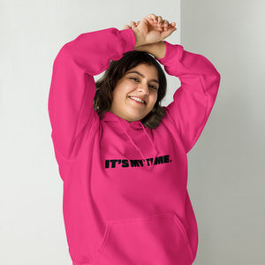 AG - Woman wearing a heliconia hoodie with 'IT'S MY TIME' text, smiling against a plain background