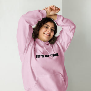 AG - Woman wearing a light pink hoodie with 'IT'S MY TIME' text, smiling against a plain background