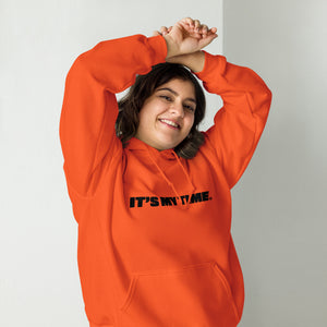AG - Woman wearing a orange hoodie with 'IT'S MY TIME' text, smiling against a plain background
