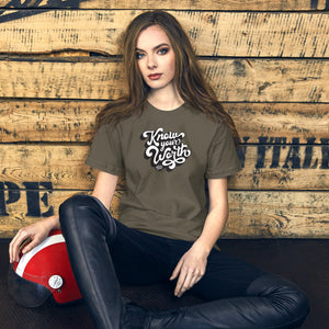 AG - Woman wearing a army t-shirt, with know your worth text, sitting against a wooden wall.