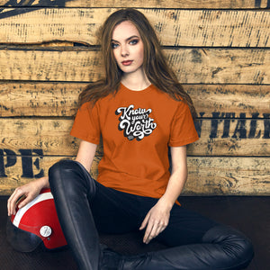 AG - Woman wearing a autumn t-shirt, with know your worth text, sitting against a wooden wall.