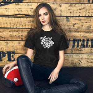 AG - Woman wearing a black t-shirt, with know your worth text, sitting against a wooden wall.