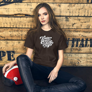 AG - Woman wearing a brown t-shirt, with know your worth text, sitting against a wooden wall.