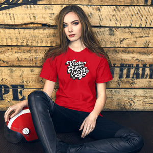 AG - Woman wearing a red t-shirt, with know your worth text, sitting against a wooden wall.