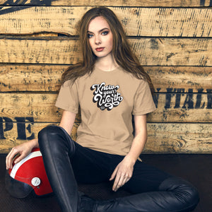 AG - Woman wearing a tan t-shirt, with know your worth text, sitting against a wooden wall.