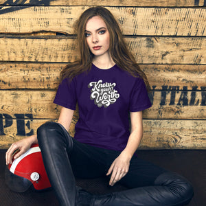AG - Woman wearing a purple t-shirt with, know your worth text, sitting against a wooden wall.