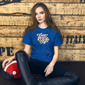 AG - Woman wearing a true royal t-shirt, with know your worth text, sitting against a wooden wall.
