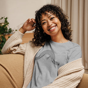 AG - Woman wearing a gray t-shirt with a musical graphic design, sitting on a couch in a cozy indoor setting.
