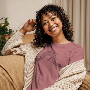 AG - Woman wearing a pink 'GEN X Musical' shirt sitting on a couch.